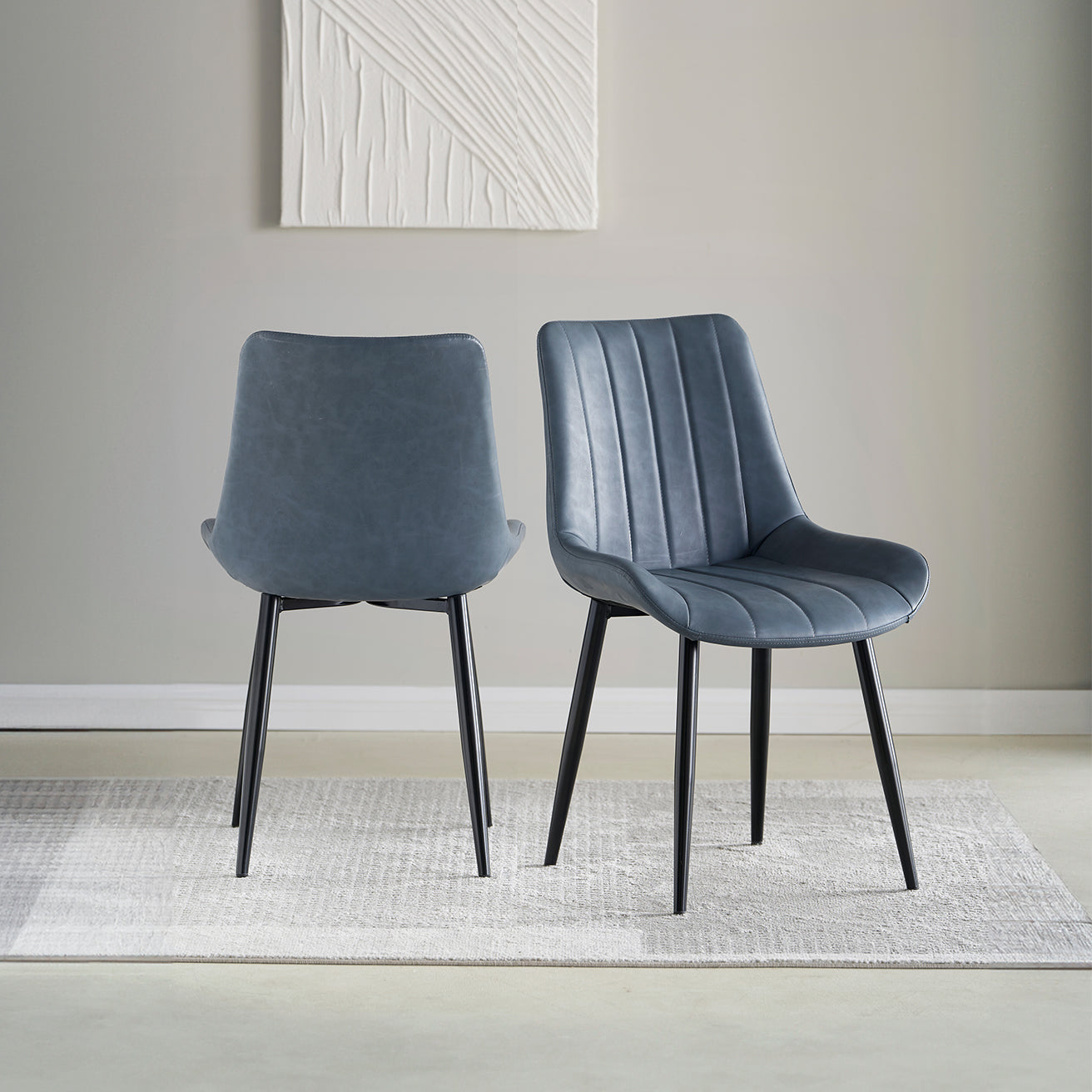 A set of two gray faux leather dining chairs with a modern design and metal legs, displayed in a room setting.