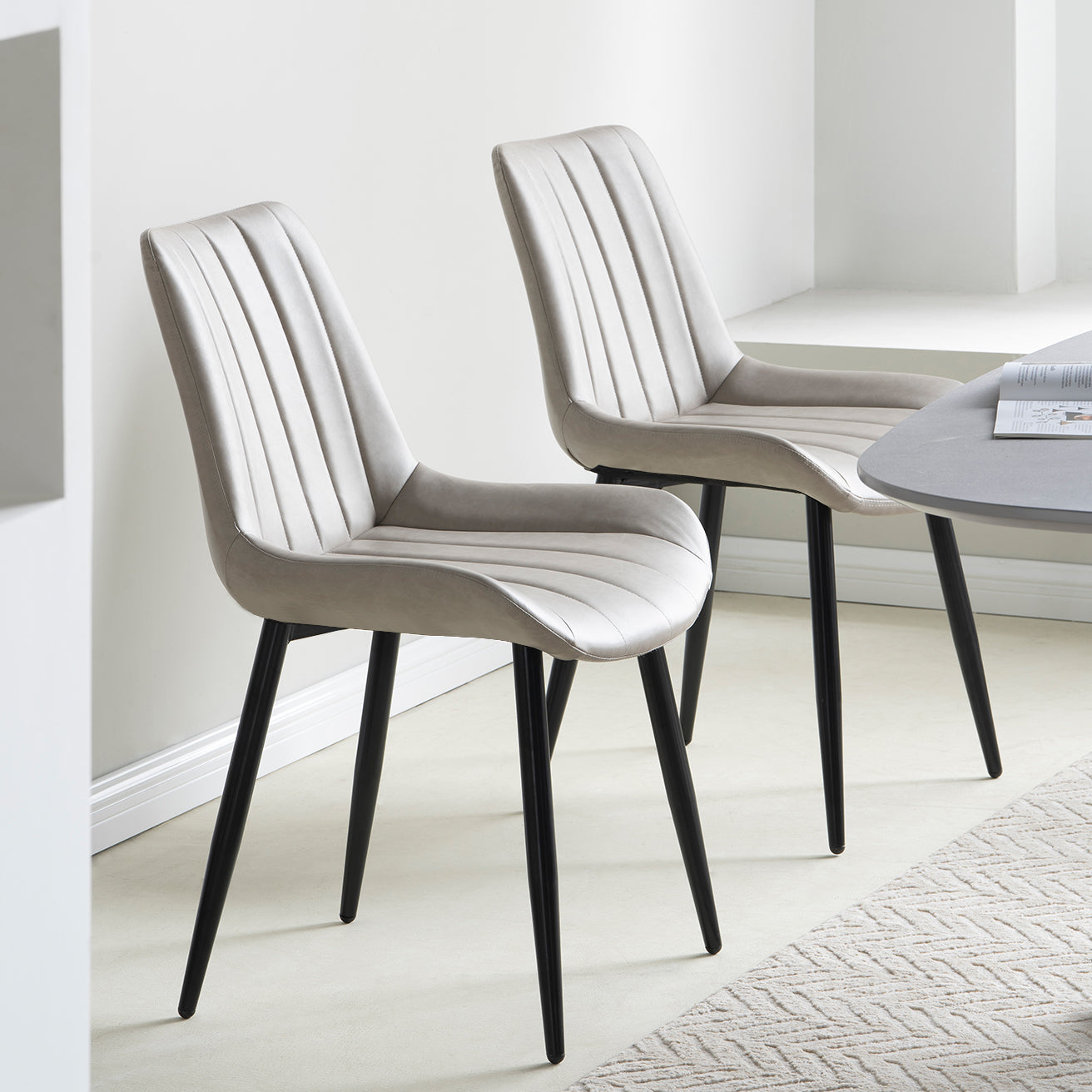 A set of two beige faux leather dining chairs with a slope design and crossed metal legs.